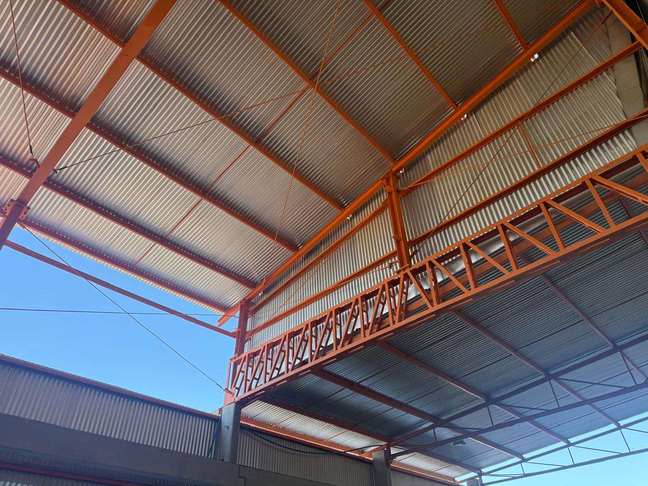 Estrutura metálica laranja com telhas instalada dentro de uma área industrial