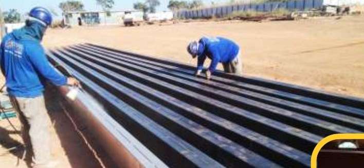 Equipe preparando e pintando perfis metálicos em área de fabricação